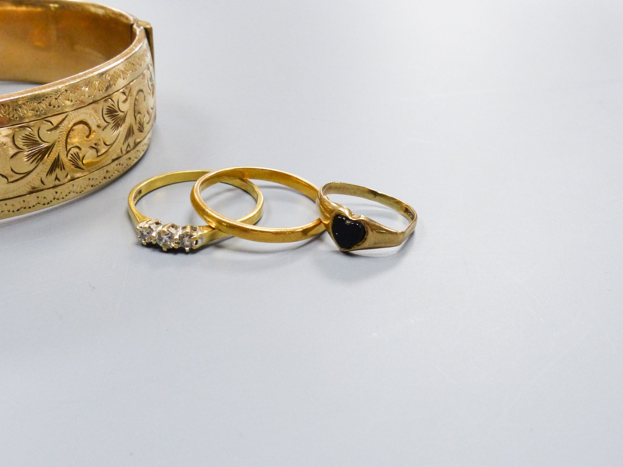 A filled 9ct gold (metal core) bangle together with a three-stone 18ct yellow gold diamond ring (gross 2.6g) a 22ct yellow gold wedding band (3.1g) and a further small gold ring and an enamelled coin pendant on chain (5)